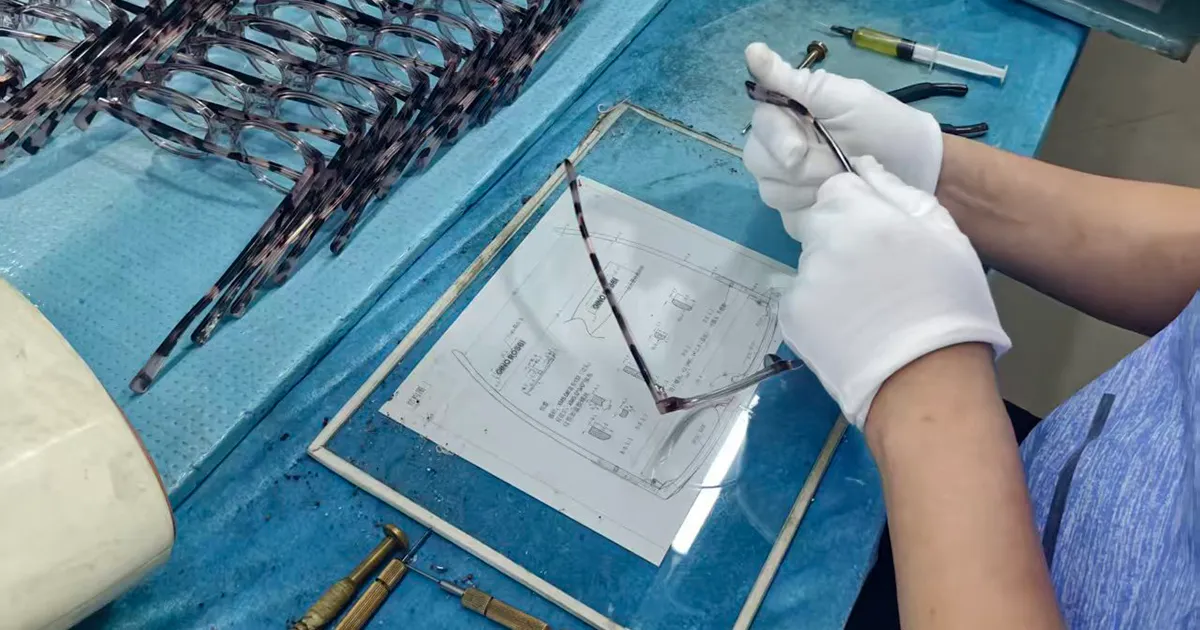 Worker in white gloves checking a custom acetate frame against its technical drawing at the VISTALUMO factory in Yiwu