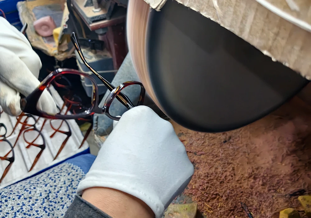 Worker in white gloves hand-polishing a tortoise acetate frame on a buffing wheel